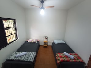 Acomodação simples, com um quarto, duas camas de solteiro, ventoinha no teto e janela com grades.