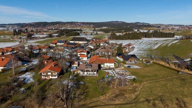 Ein Wohngebiet mit Häusern, einige mit roten Dächern, umgeben von offenen Feldern und einer in der Ferne liegenden Stadt.