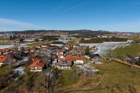 Área residencial com casas, algumas com telhados vermelhos, cercada por campos abertos e uma cidade ao longe.