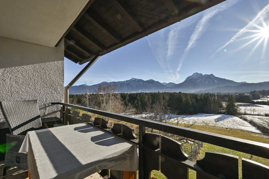 A balcony with a table and chairs, overlooking a mountainous landscape with snow-covered fields.