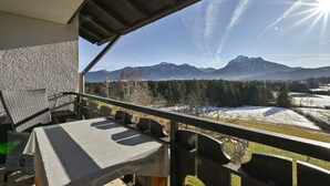 Ein Balkon mit Tisch und Stühlen, mit Blick auf eine gebirgige Landschaft und schneebedeckte Felder.