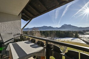 Varanda com mesa e cadeiras, com vista para uma paisagem montanhosa e campos cobertos de neve.