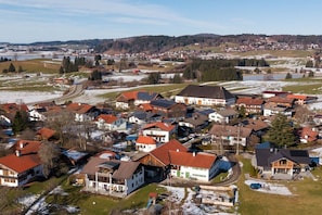 Een woonwijk met huizen, waarvan sommigen zonnepanelen hebben, omgeven door open velden en een in de verte gelegen stad.