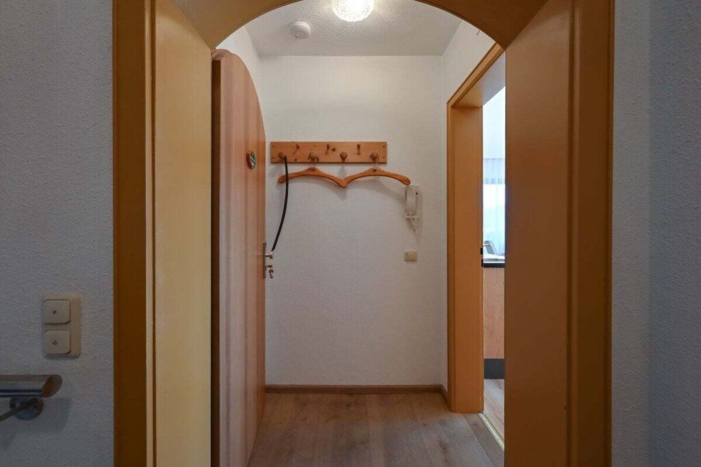 Un couloir étroit avec un cadre de porte en bois, un porte-manteau et un interrupteur sur le mur.