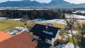 Ein Wohngebiet mit einem Haus, das ein geneigtes Dach, einen umzäunten Garten und einen Blick auf schneebedeckte Berge bietet.