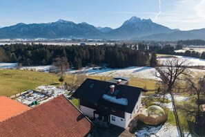Bairro residencial com uma casa de telhado inclinado, quintal cercado e vista para montanhas cobertas de neve.
