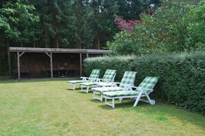 A grassy outdoor area with a row of white lounge chairs with green cushions, a covered seating area, and a dense hedge. - Heather beetle - "Holiday home hedgehog" (Kirchlinteln-Bendingbostel)