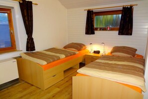 Une petite chambre confortable, avec deux lits simples, une table de chevet avec une lampe, une fenêtre avec des rideaux et un radiateur.