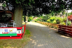 A paved pathway with a red bench and a sign labeled 'LandUrlauf' on the left. - Heather beetle - "Holiday home hedgehog" (Kirchlinteln-Bendingbostel)