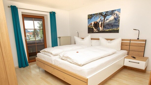 Een slaapkamer met een bed, een nachtkastje, een raam met gordijnen en een schilderij aan de muur.
