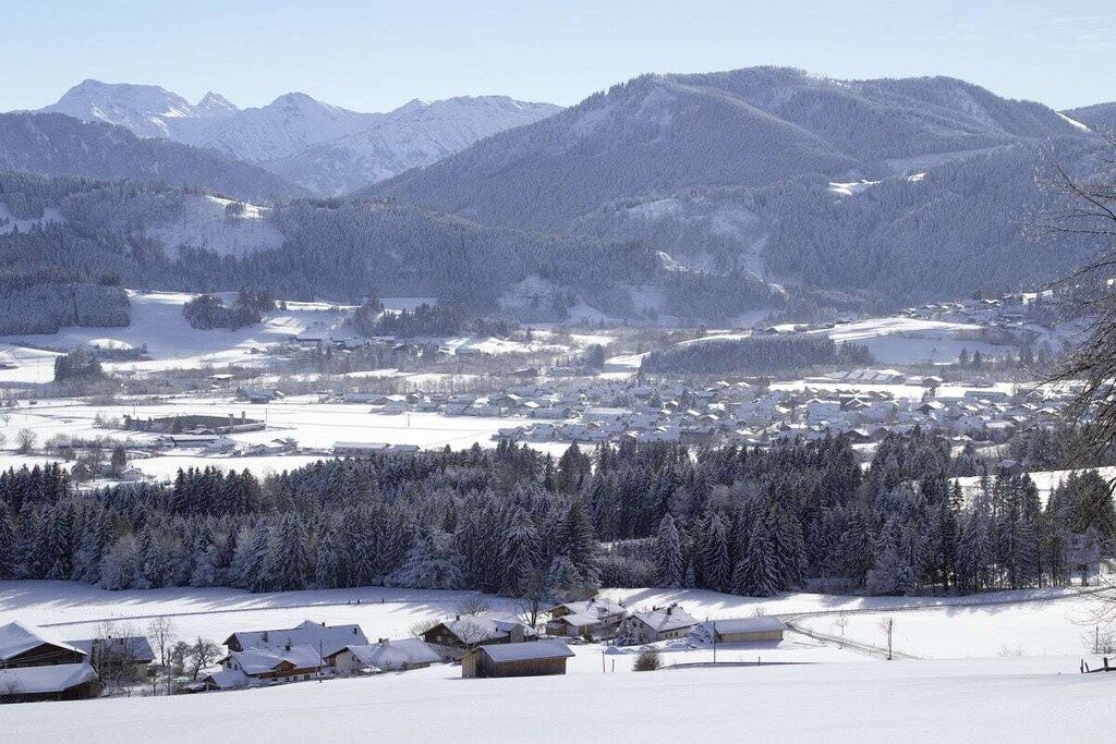 Vila coberta de neve, com casas e montanhas ao fundo.
