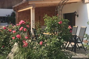 Un espace extérieur aménagé avec une table et des chaises, entouré de fleurs roses en pleine floraison.