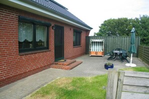 Een bakstenen huis met een terras, een groene deur en een omheind gebied met tuinmeubilair.