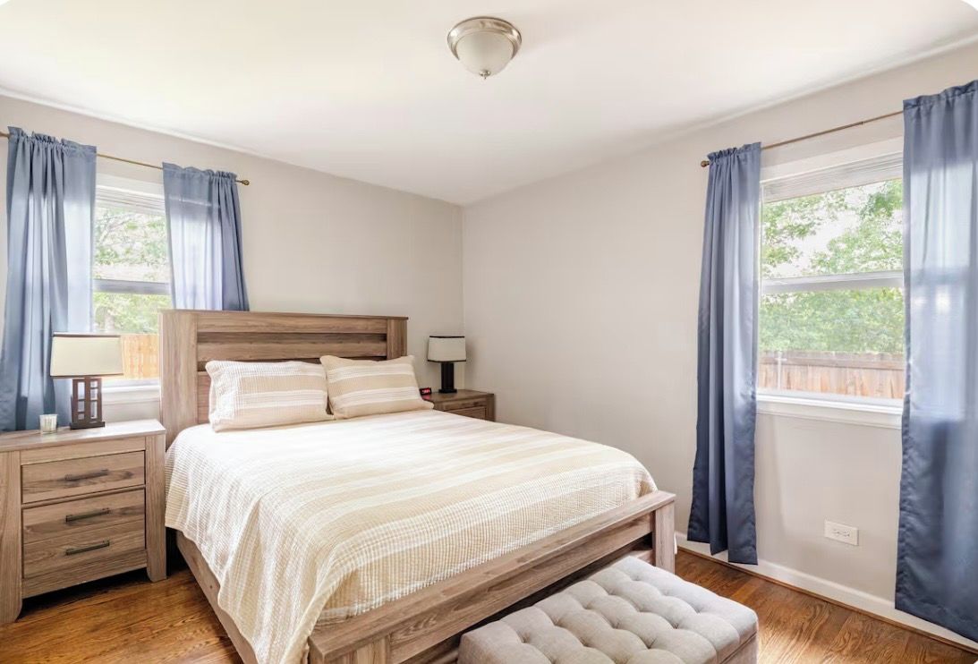 Une chambre à coucher avec un lit en bois, une table de chevet, une commode et une fenêtre avec des rideaux.