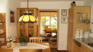 A kitchen with wooden cabinets, a dining table with chairs, a hanging light fixture, and a view through a glass door to an outdoor area. - Holiday apartment with 1 bedroom (Gummersbach - Lieberhausen)