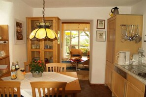 A kitchen with wooden cabinets, a dining table with chairs, a hanging light fixture, and a view through a glass door to an outdoor area. - Holiday apartment with 1 bedroom (Gummersbach - Lieberhausen)