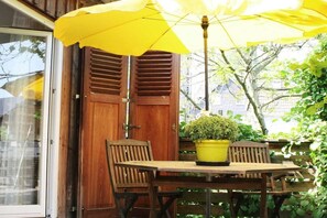 A wooden door with shutters, a table with a potted plant, and a yellow umbrella. - Holiday apartment with 1 bedroom (Gummersbach - Lieberhausen)