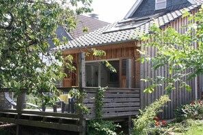 Una casa de madera con balcón, jardín cercado y terraza de madera.