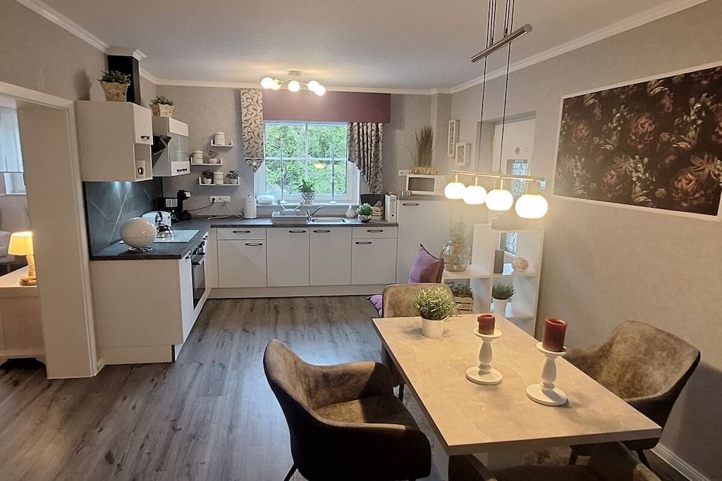A modern kitchen with white cabinetry, a dining table with chairs, and a window with curtains.