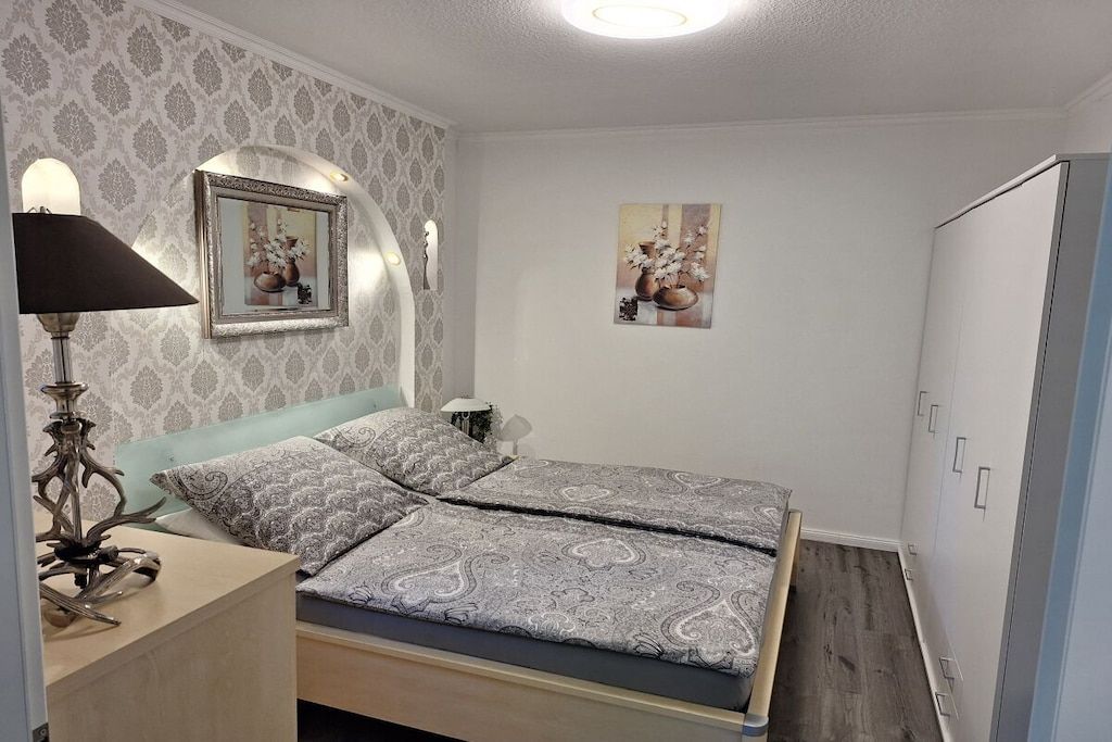 A bedroom with a bed, a bedside lamp, a mirror, and a wardrobe.