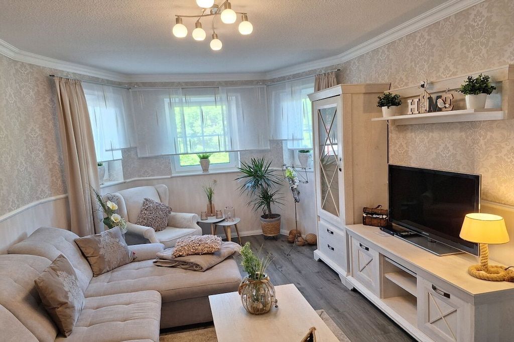 Una sala de estar con sofá, televisión y plantas decorativas.
