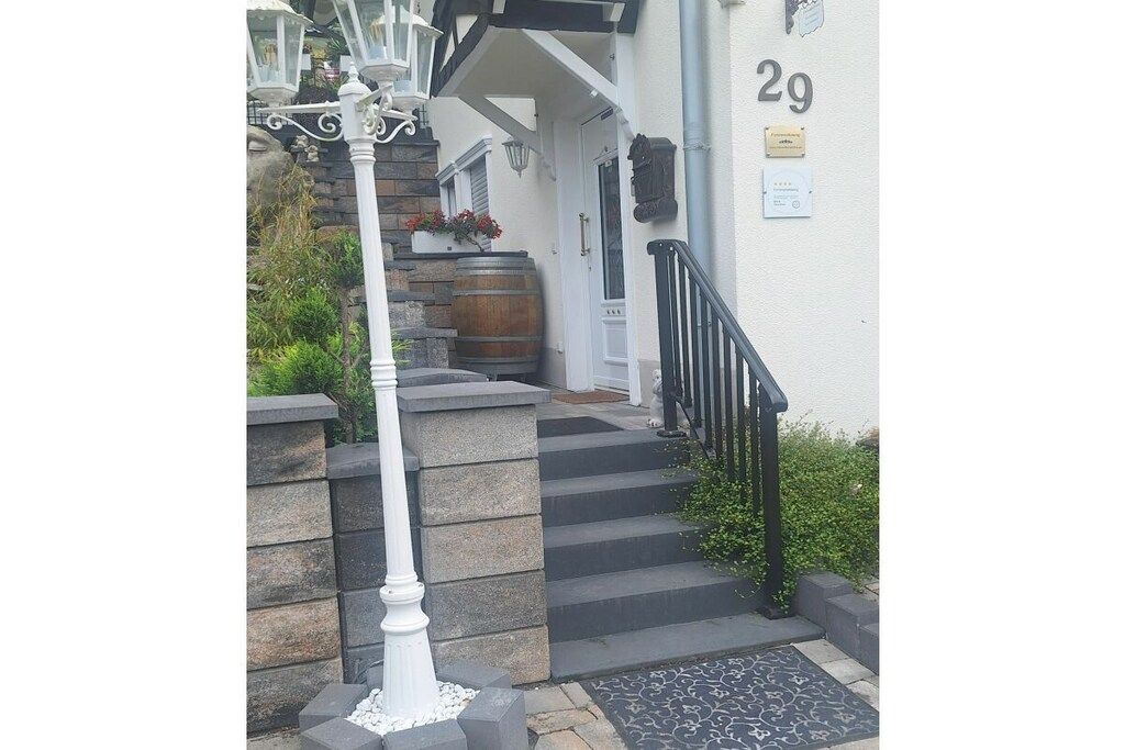 A white building with a stone staircase leading to a door, a black metal railing, and a white street lamp.