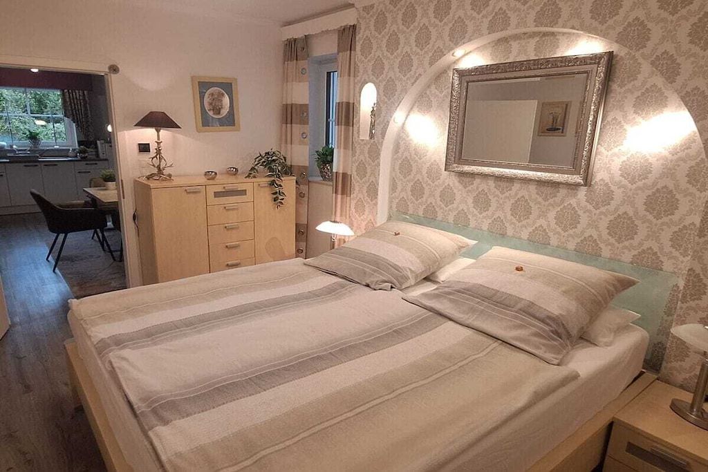 A hotel room with a bed, bedside table, lamp, dresser, and a mirror.