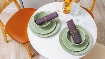 A compact dining area with a white table, two wicker chairs, a bench, and a compact refrigerator.