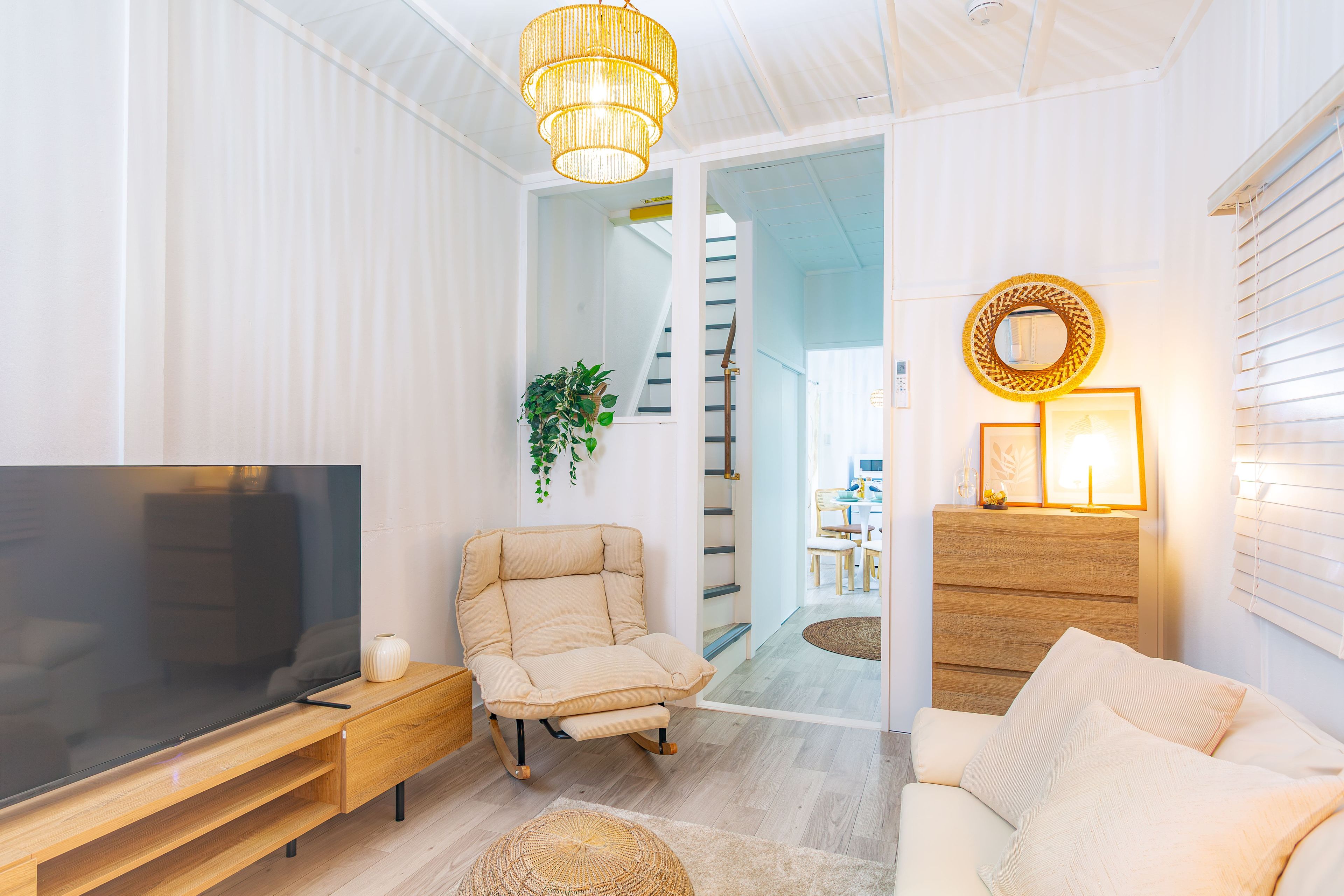 Una sala moderna con un televisor de pantalla plana, un sillón color beige, una mesa de centro de madera y un sofá.