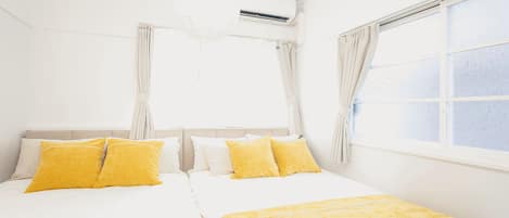 Habitación de hotel con dos camas, ropa de cama blanca y almohadas amarillas.