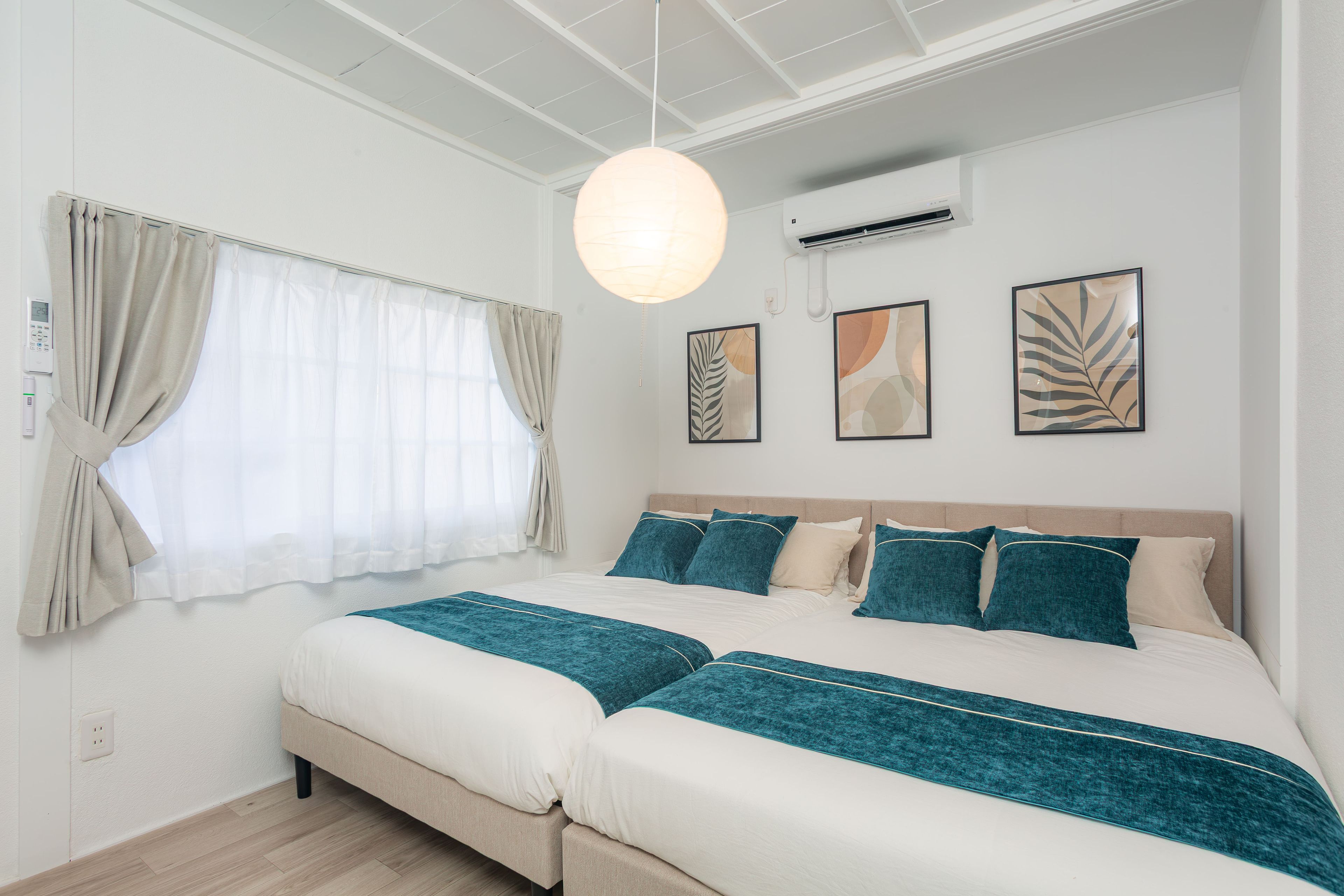 A bedroom with a large bed, a bedside table, a wall-mounted air conditioner, and a window with curtains.