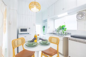 Une cuisine moderne avec des meubles blancs, un four à micro-ondes, un évier et un coin repas comprenant une table ronde et des chaises en osier.