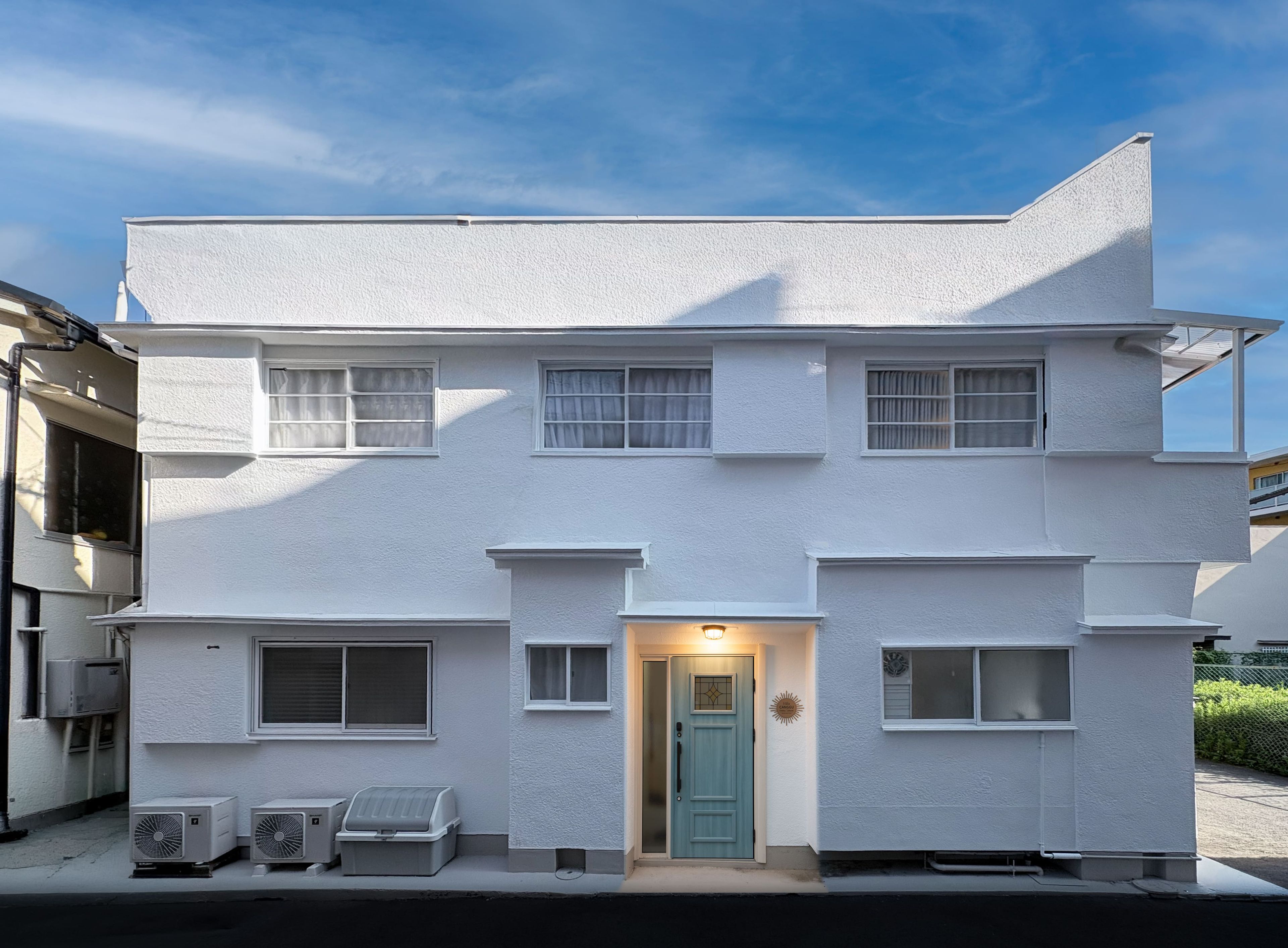 A two-story building with a flat roof, a central entrance with a door, and two air conditioning units on the ground floor.