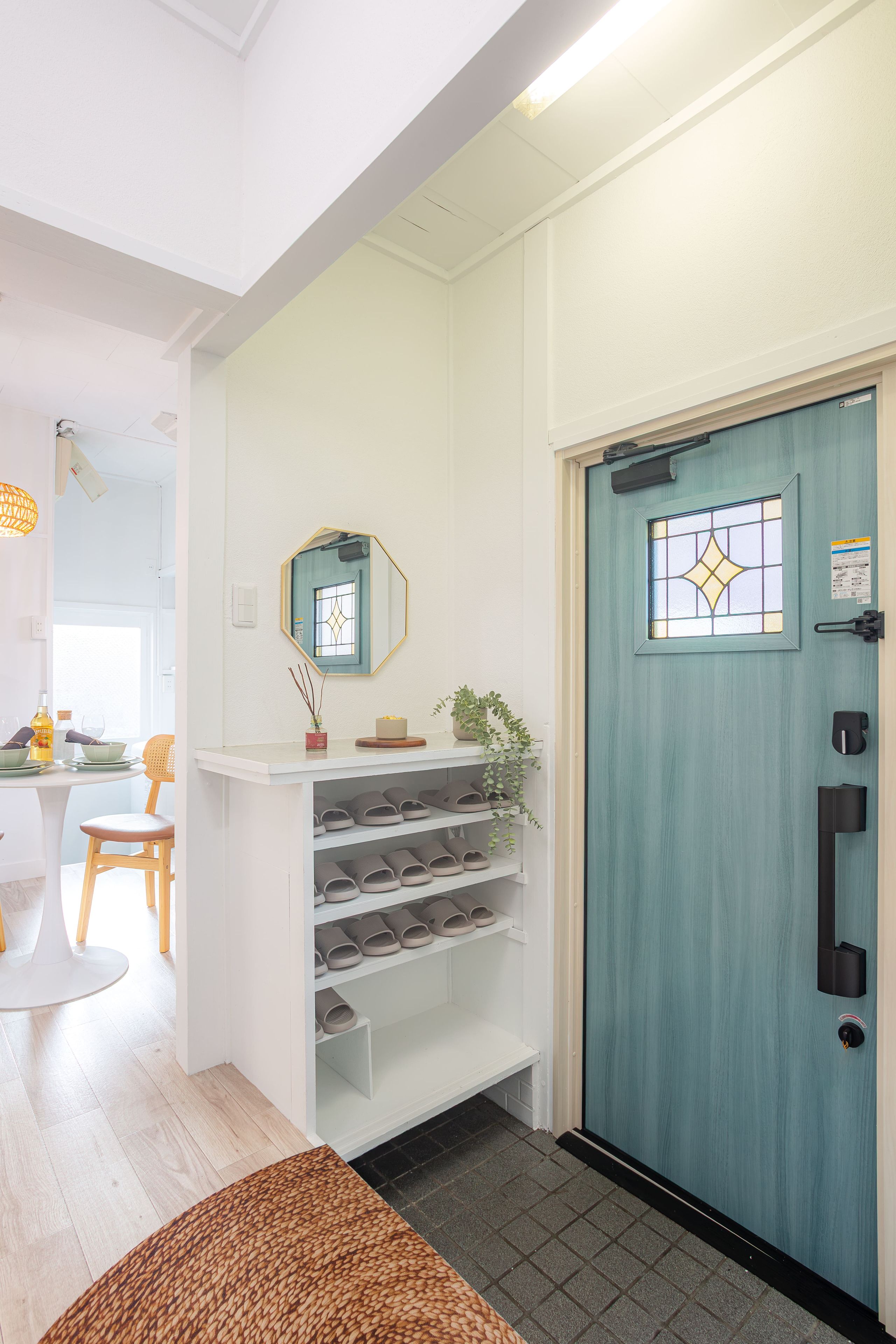 A room with a white wall, a blue door with a window, and a white shelf with shoes.