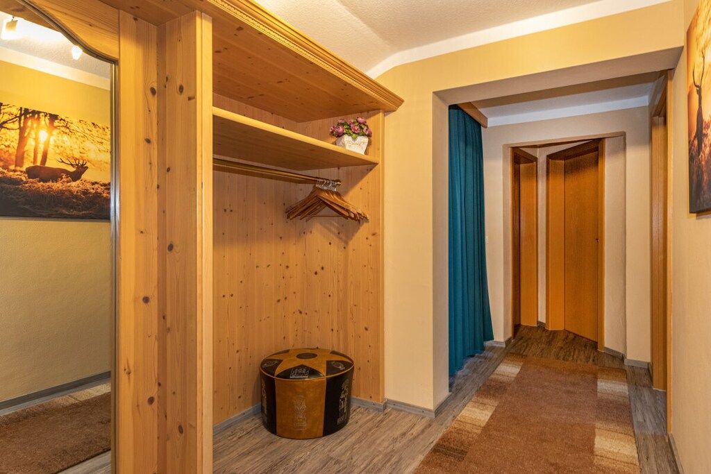 Un pasillo con paneles de madera, un perchero, un taburete redondo y un cuadro en la pared.