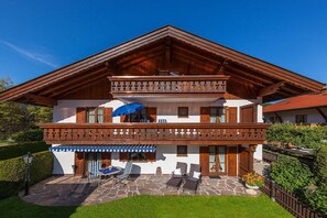 A two-story chalet with a balcony, stone patio, and outdoor seating area. - Karwendele Echo - Edelweiss (Mittenwald)