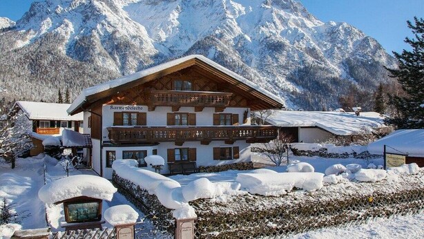 A traditional chalet-style building with a wooden facade, multiple balconies, and a snow-covered landscape with mountains in the background. - Karwendele Echo - Edelweiss (Mittenwald)