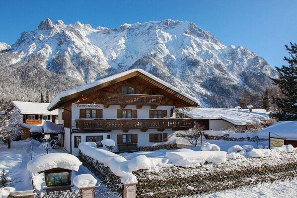A traditional chalet-style building with a wooden facade, multiple balconies, and a snow-covered landscape with mountains in the background. - Karwendele Echo - Edelweiss (Mittenwald)