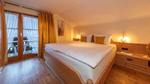 A hotel room with a large bed, wooden headboard, a nightstand, and a window with curtains. - Karwendele Echo - Edelweiss (Mittenwald)