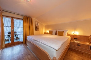 A hotel room with a large bed, wooden headboard, a nightstand, and a window with curtains. - Karwendele Echo - Edelweiss (Mittenwald)