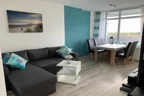 A modern living room with a sofa, coffee table, and dining area. - Holiday apartment with 2 bedrooms (Heiligenhafen)