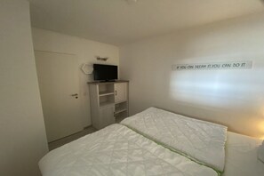 A bedroom with a bed, a television on a stand, a wardrobe, and a motivational quote on the wall. - Holiday apartment with 2 bedrooms (Heiligenhafen)