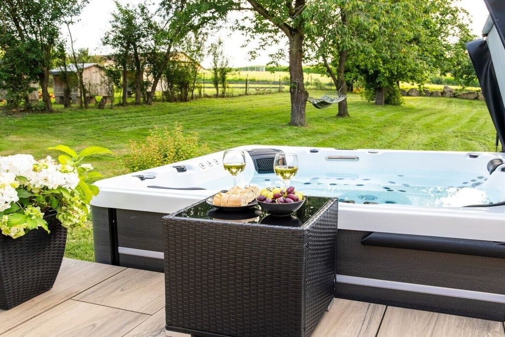 A hot tub with a wicker table and potted plants in a garden setting.