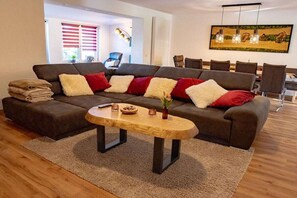 Een moderne woonkamer met een modulaire bank, een houten salontafel en een eethoek met stoelen.