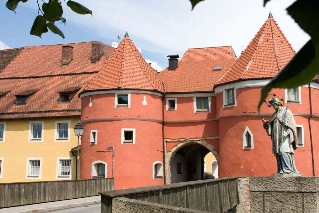 Un edificio histórico con techo de tejas rojas, una estatua y una valla de madera.