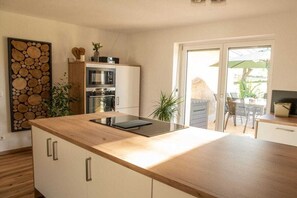 Une cuisine moderne dotée d’un îlot central, d’appareils électroménagers intégrés et d’un coin repas avec une porte vitrée donnant sur l’extérieur.