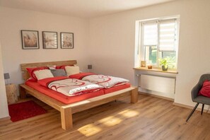 Une chambre avec un lit en bois, un tapis rouge, une fenêtre avec des stores et une chaise.