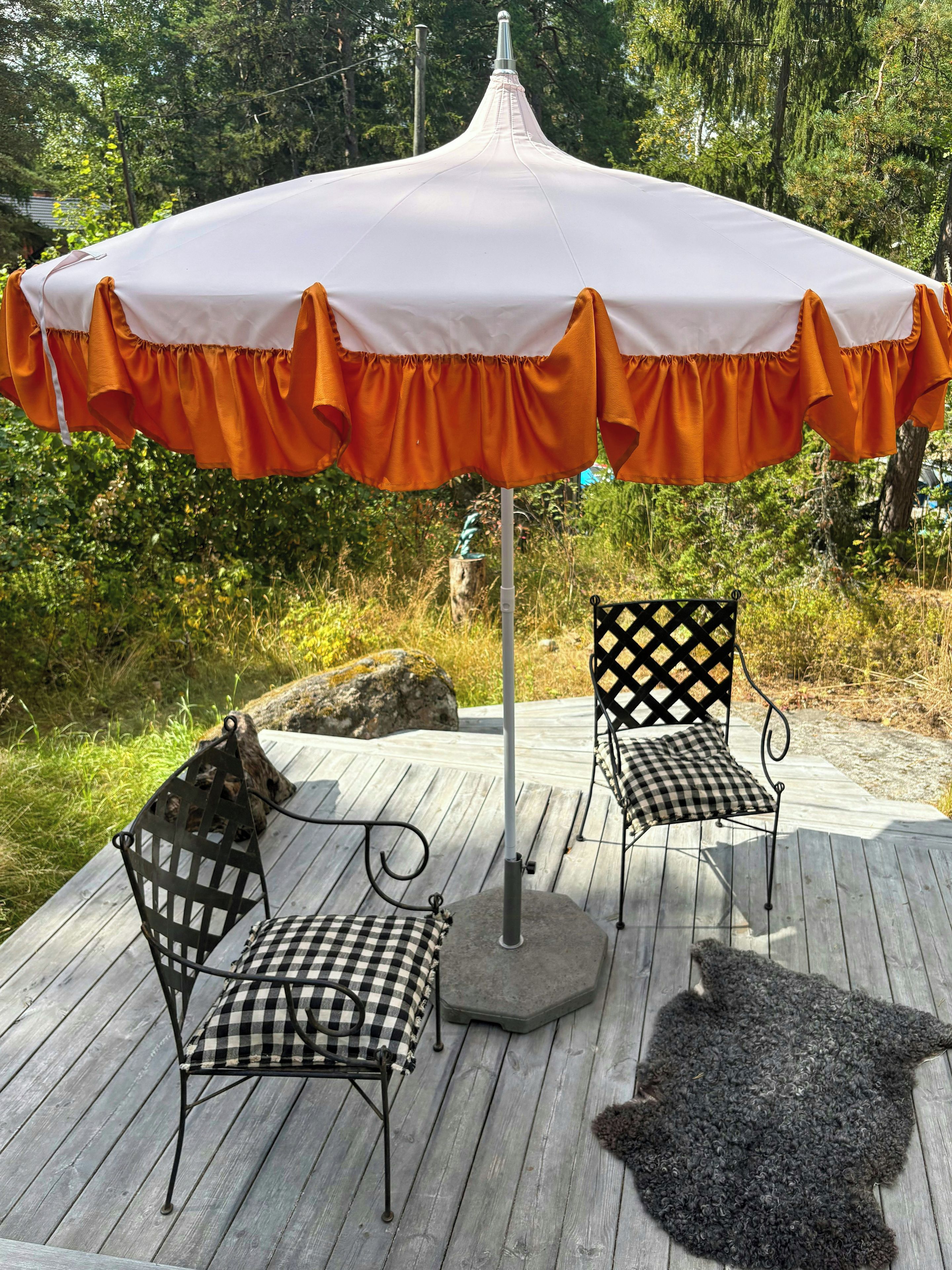 An outdoor seating area with a white umbrella, two checkered chairs, and a rug.