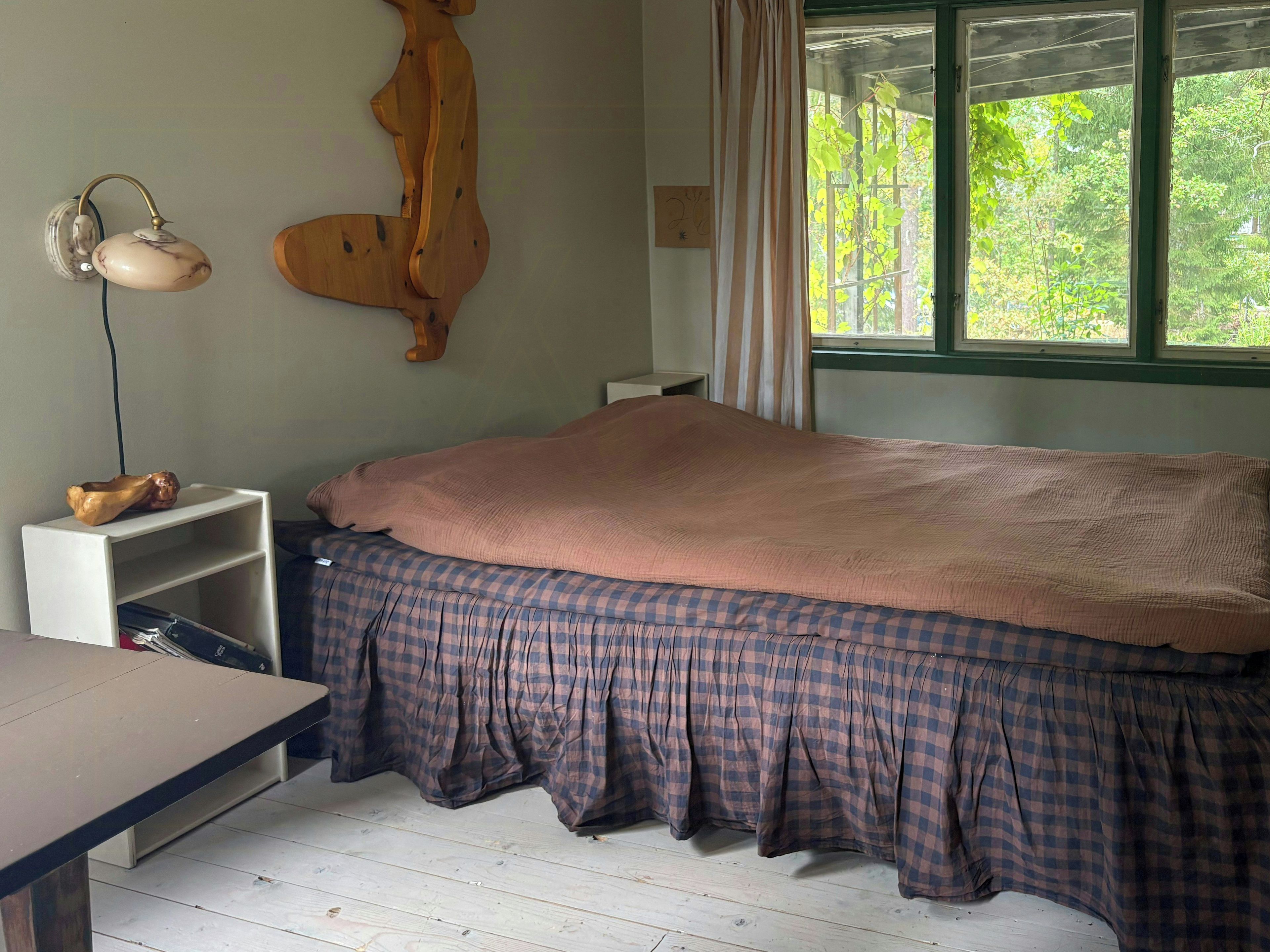Een slaapkamer met een bed, bureau, lamp en een raam met gordijnen.