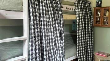 Una camera da letto con un letto a castello, tende a quadretti, un piccolo armadietto in legno con oggetti decorativi e un tappeto a motivi.